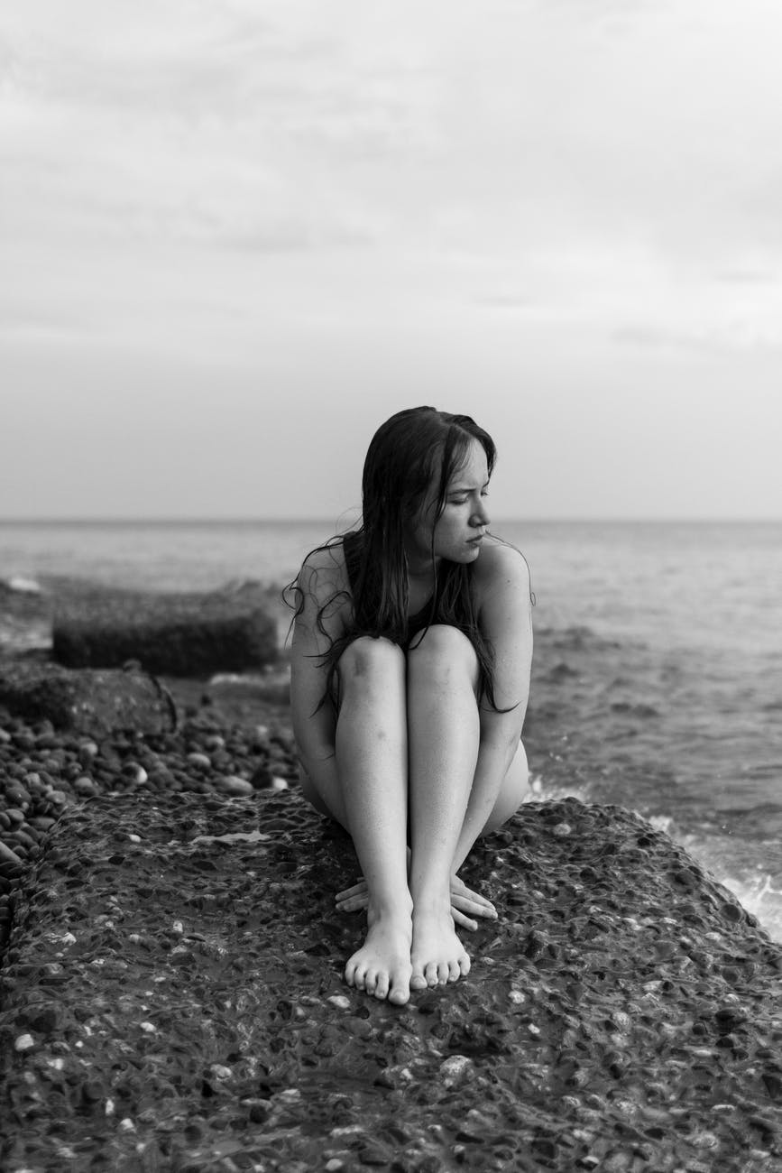 young naked woman sitting curled up on stony beach
