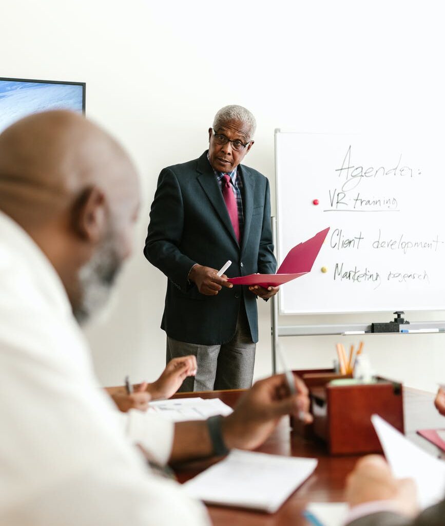 a man in black suit standing in front of his colleagues