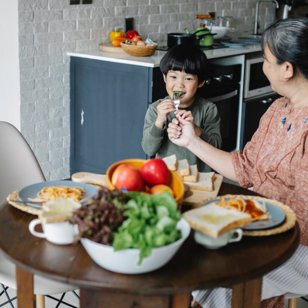 cheerful little asian boy having breakfast with kind grandmother at home