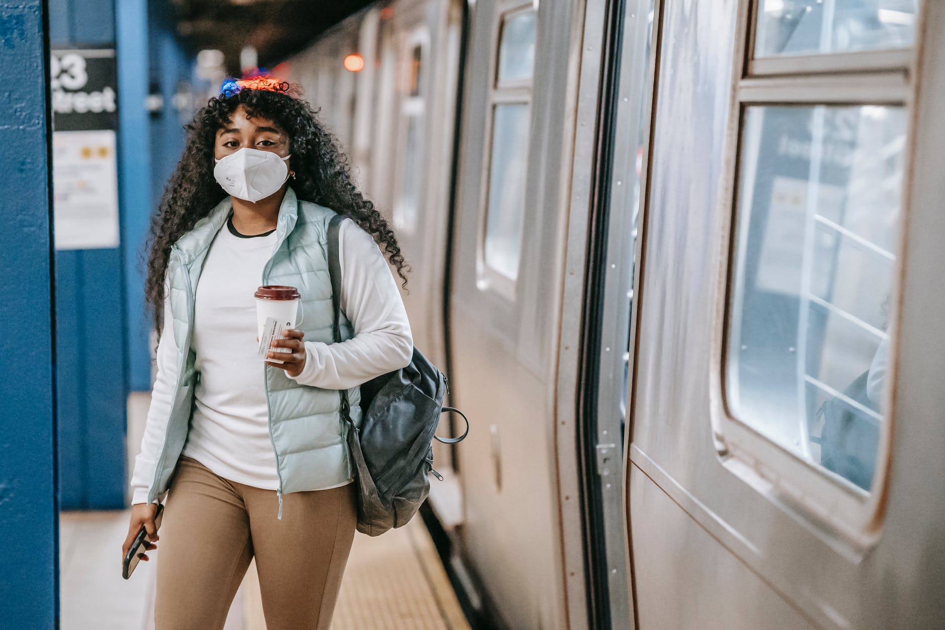 calm black woman with coffee wearing medical mask standing in metro