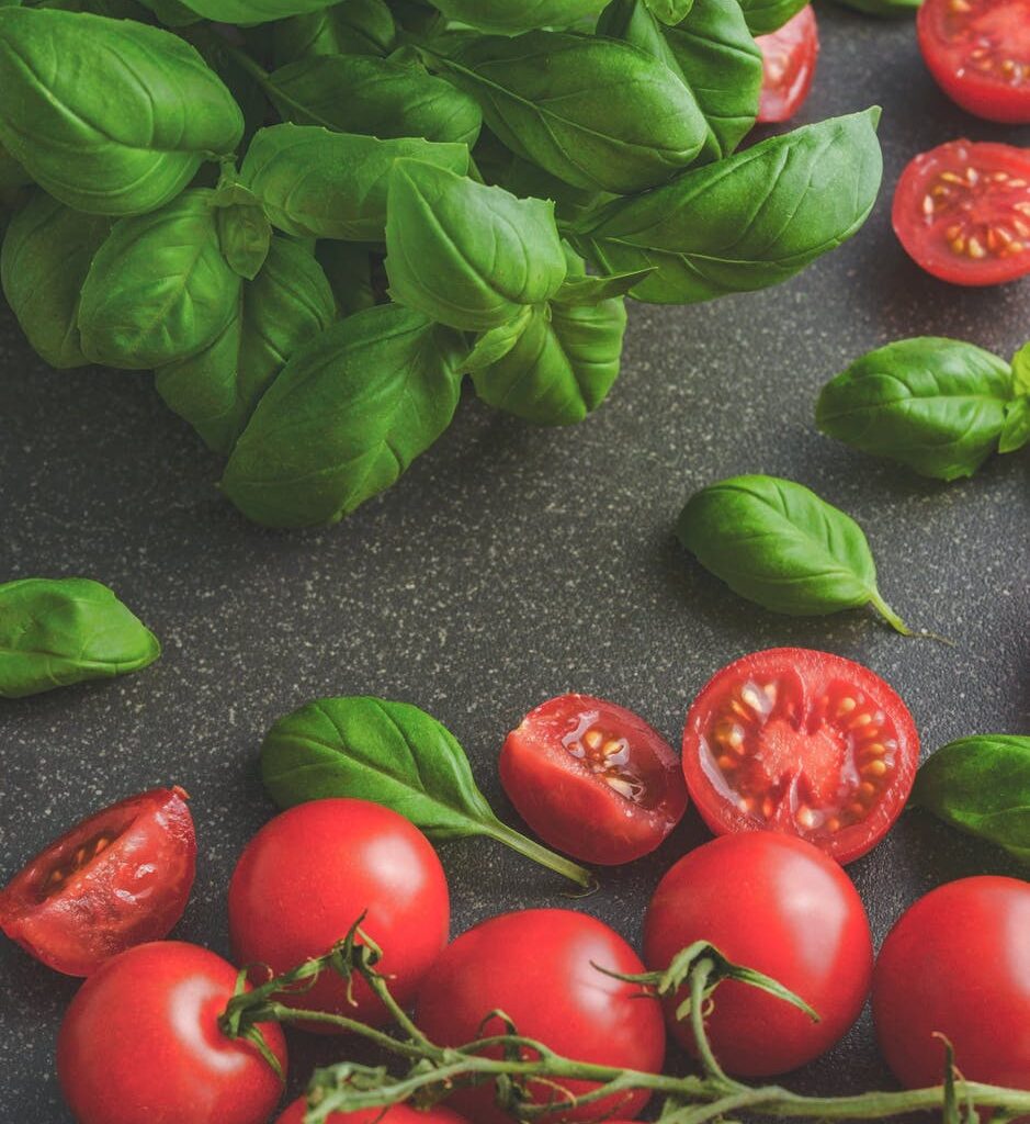 photography of tomatoes near basil leaves