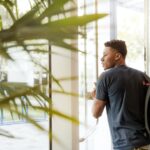 man looking outside window carrying black and brown backpack while holding his hand on window