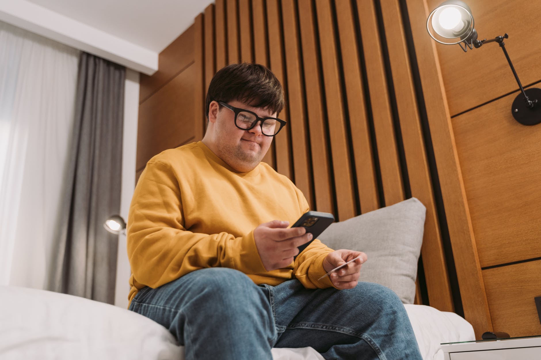 man in yellow sweater holding black smartphone and credit card