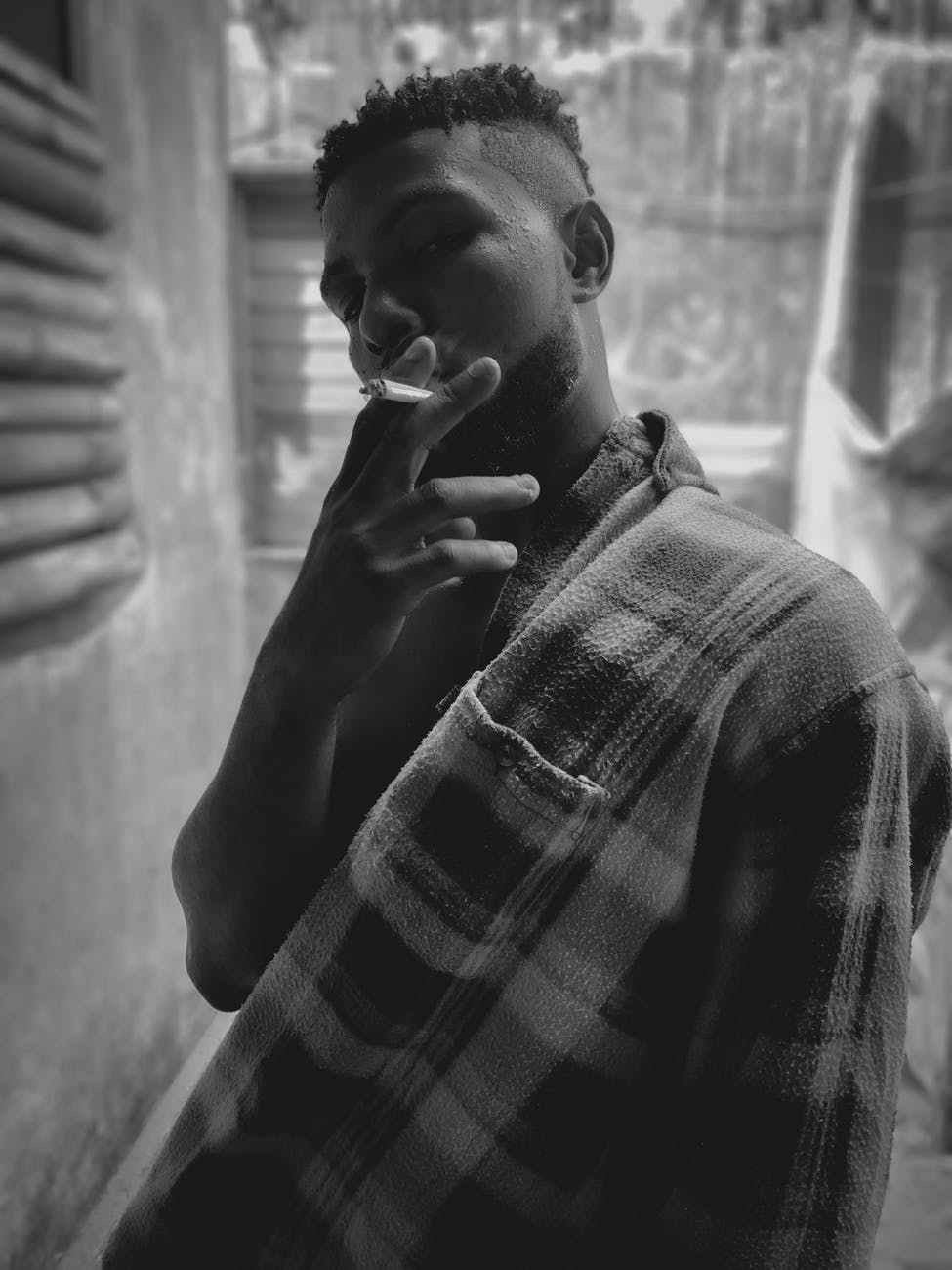 a grayscale photo of a man in plaid long sleeves smoking cigarette
