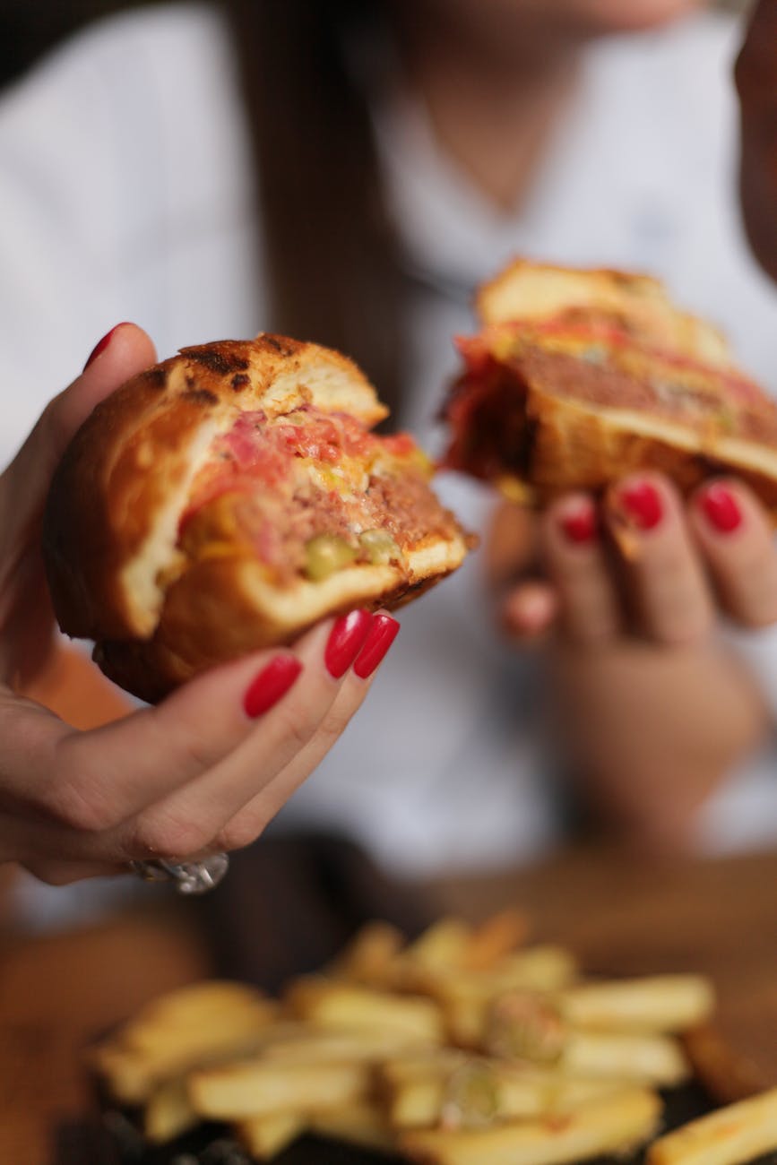 person holding burger with ham and cheese