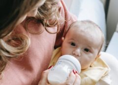 cute newborn drinking milk from bottle in hands of crop mom