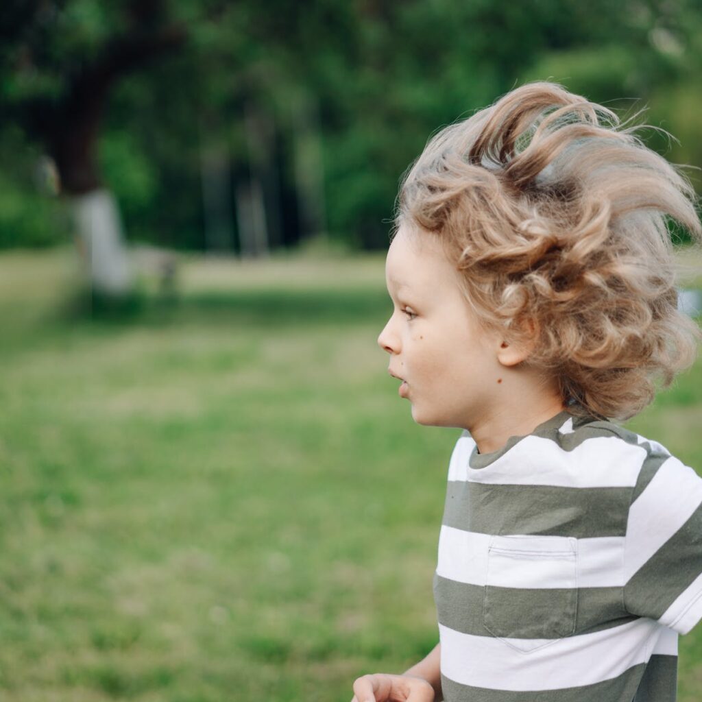 a side view of a young boy in striped shirt running at the park