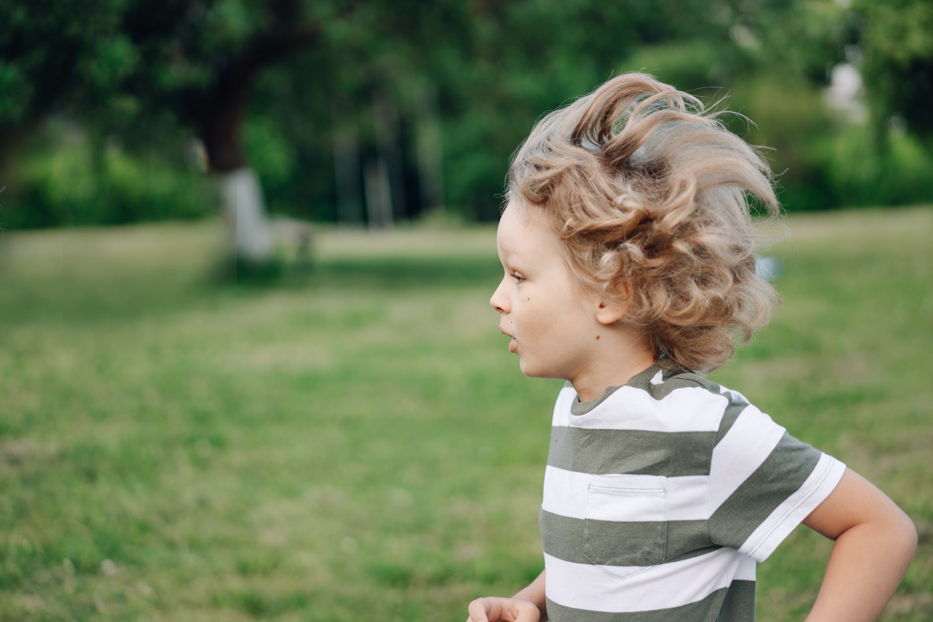 a side view of a young boy in striped shirt running at the park