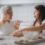 pensive grandmother with granddaughter having interesting conversation while cooking together in light modern kitchen