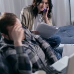 woman on the phone holding paperwork beside a man in deep thoughts