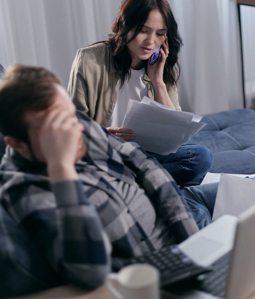 woman on the phone holding paperwork beside a man in deep thoughts