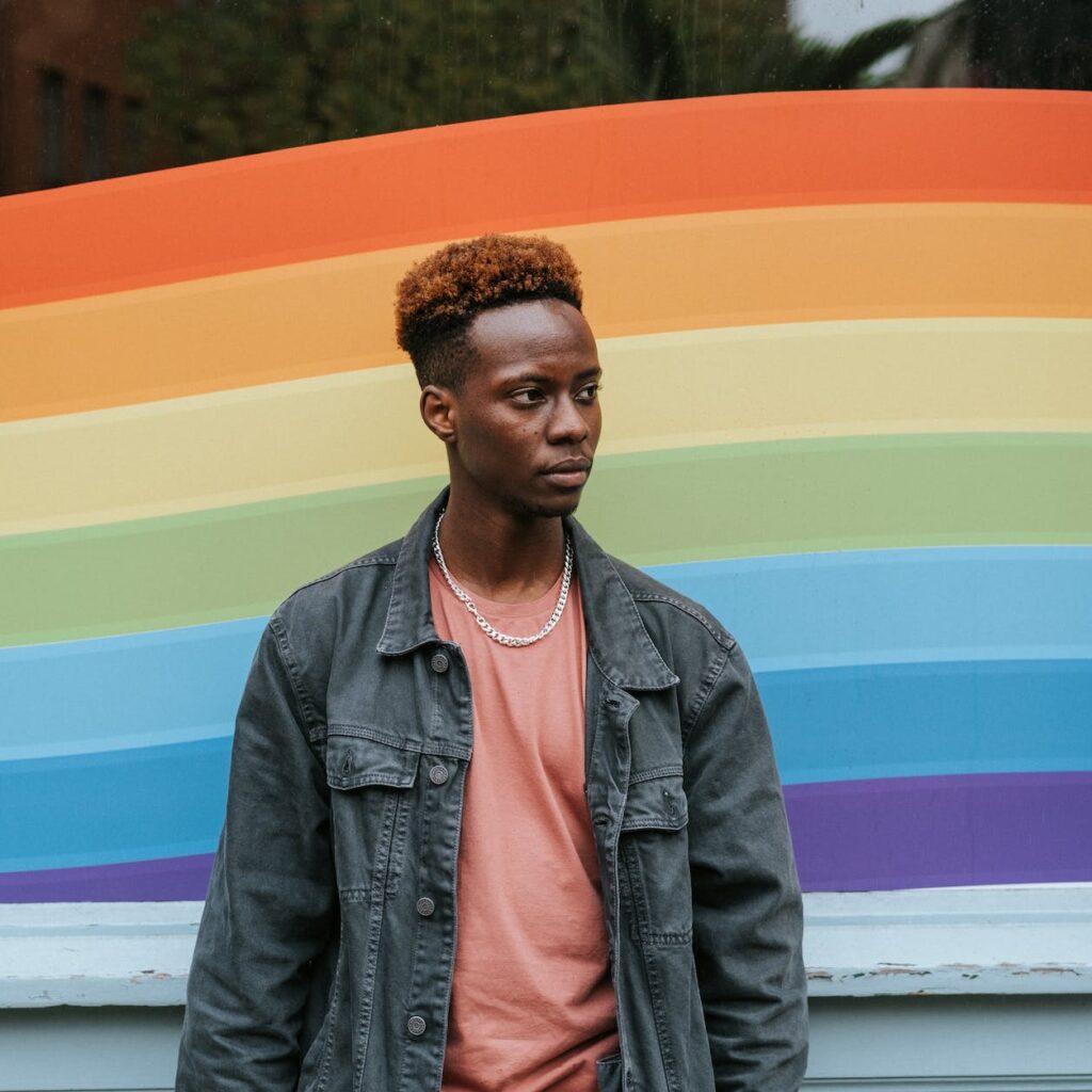 contemplative black man standing against window painted in lgbt colors